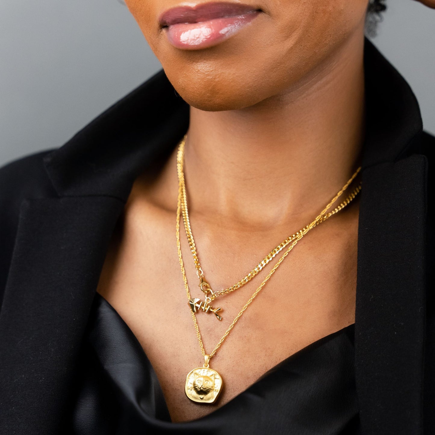female model wearing the mars fish bone necklace in 18k gold vermeil and the lars reversible cat coin necklace in 18k gold vermeil
